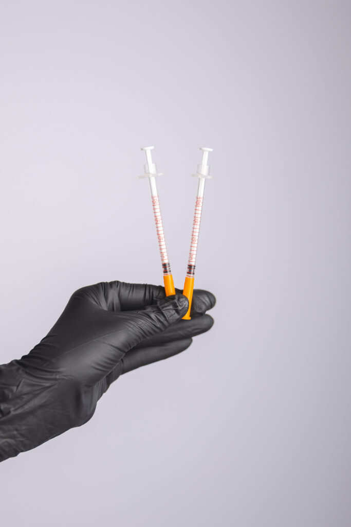 Aesthetic injector holding two syringes filled with cosmetic injectable treatment product against a neutral background at Pine & River Aesthetics.