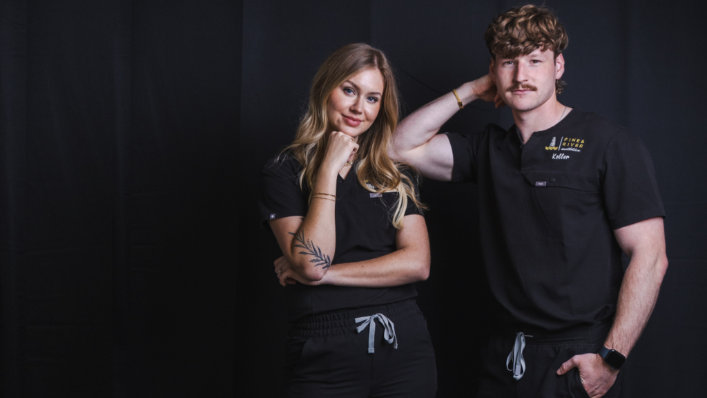 Pine & River Aesthetics team members posing together in black scrubs against a dark studio backdrop in Little Rock, Arkansas.