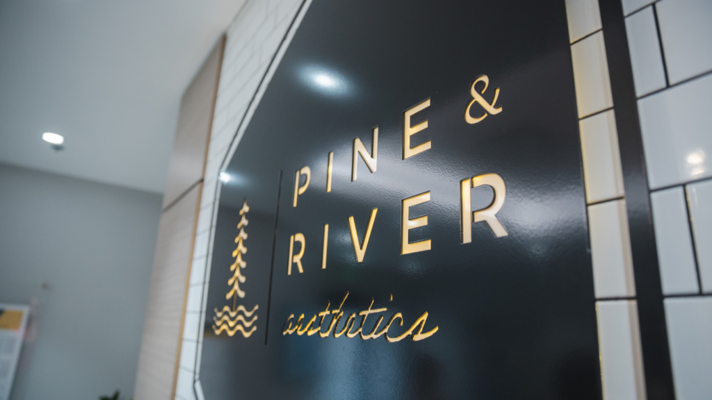 Illuminated Pine & River Aesthetics logo sign mounted on a white subway tile wall inside the luxury med spa in Little Rock, Arkansas.