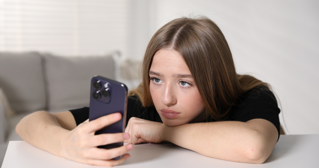 Teen girl looking at her phone while resting her head on her arm.